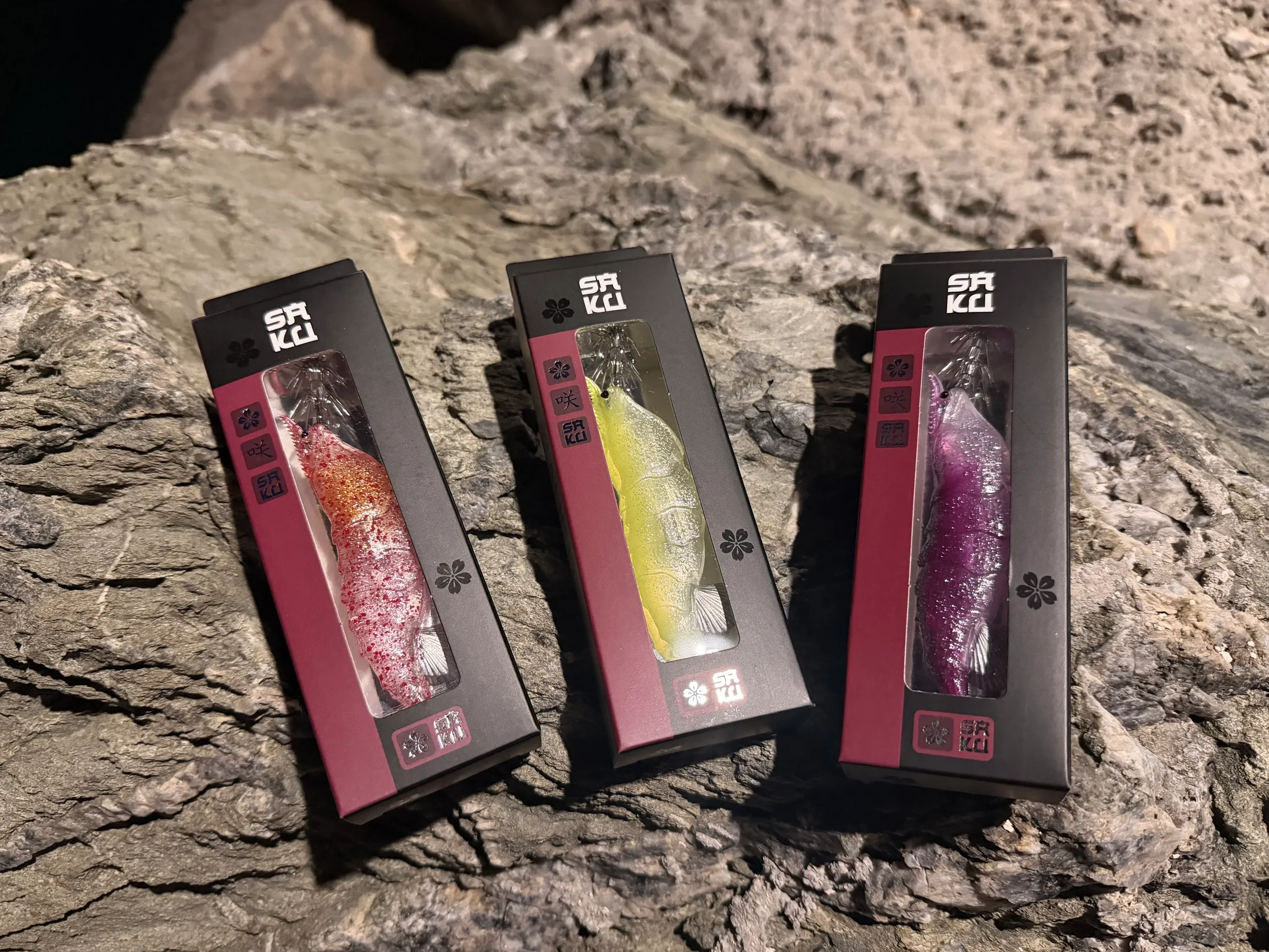 Three boxed TAFROS squid jigs arranged on rock showing the Saku retail packaging